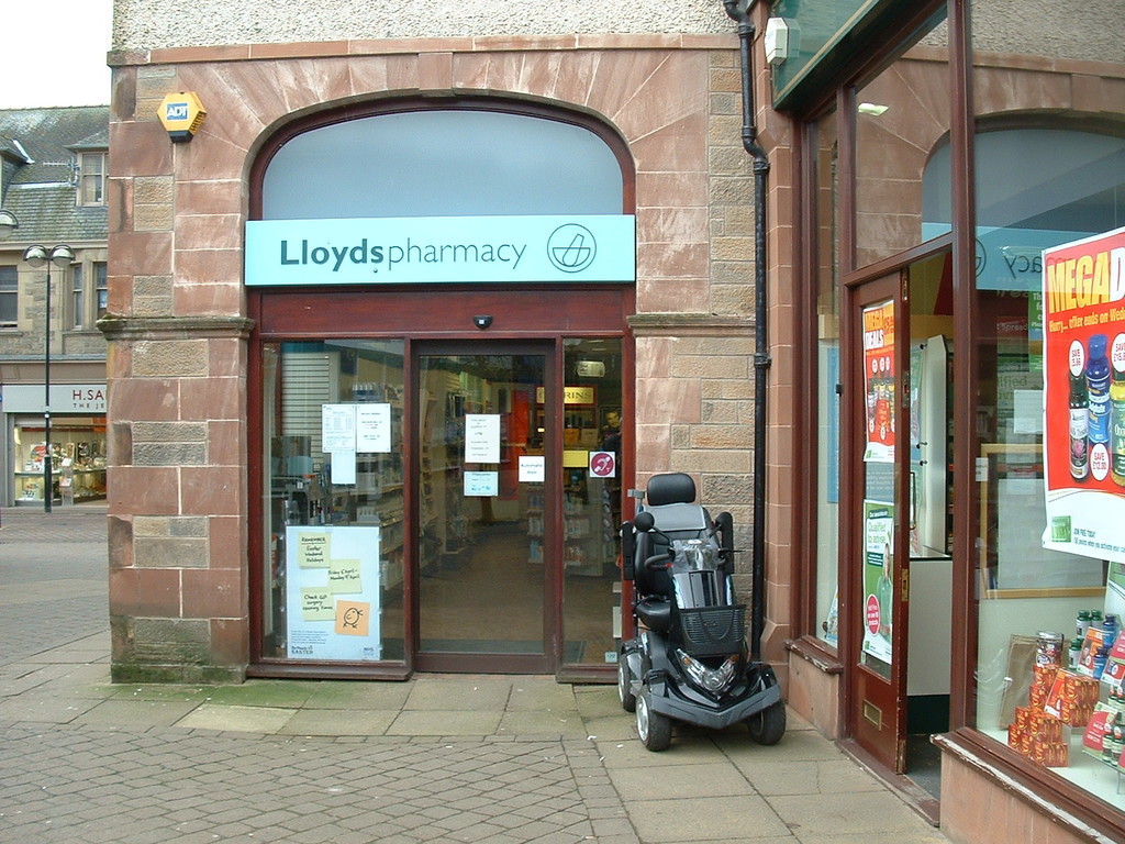 Eine Apotheke mit einem vor ihr geparkten Fahrzeug und einem Gebäude, das links sichtbar ist.