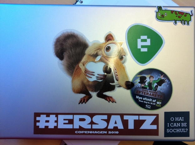 Ein Laptop und ein Buch sind auf einem Tisch platziert, mit verschiedenen Stickern auf dem Laptop.