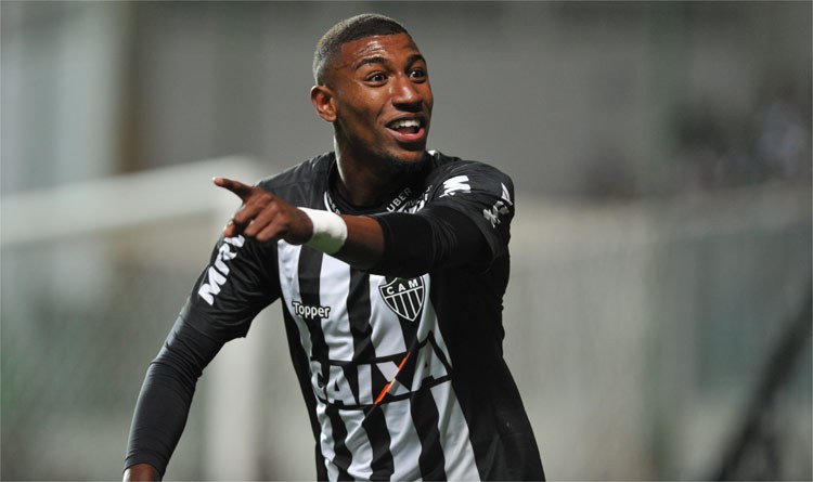 Ein Fussballspieler in einem schwarz-weiss gestreiftem Trikot lacht beim Feiern eines Tors, mit einem unscharfen Hintergrund, der den Moment betont.