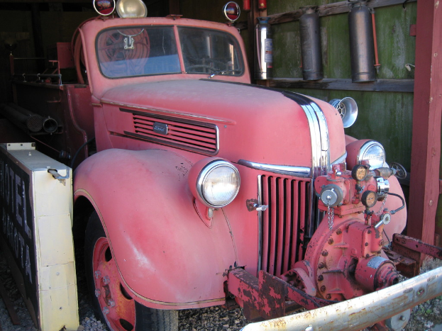 Ein Kraftfahrzeug steht auf einem steinbedeckten Boden, neben ihm sind zwei Feuerlöscher an der Wand montiert.