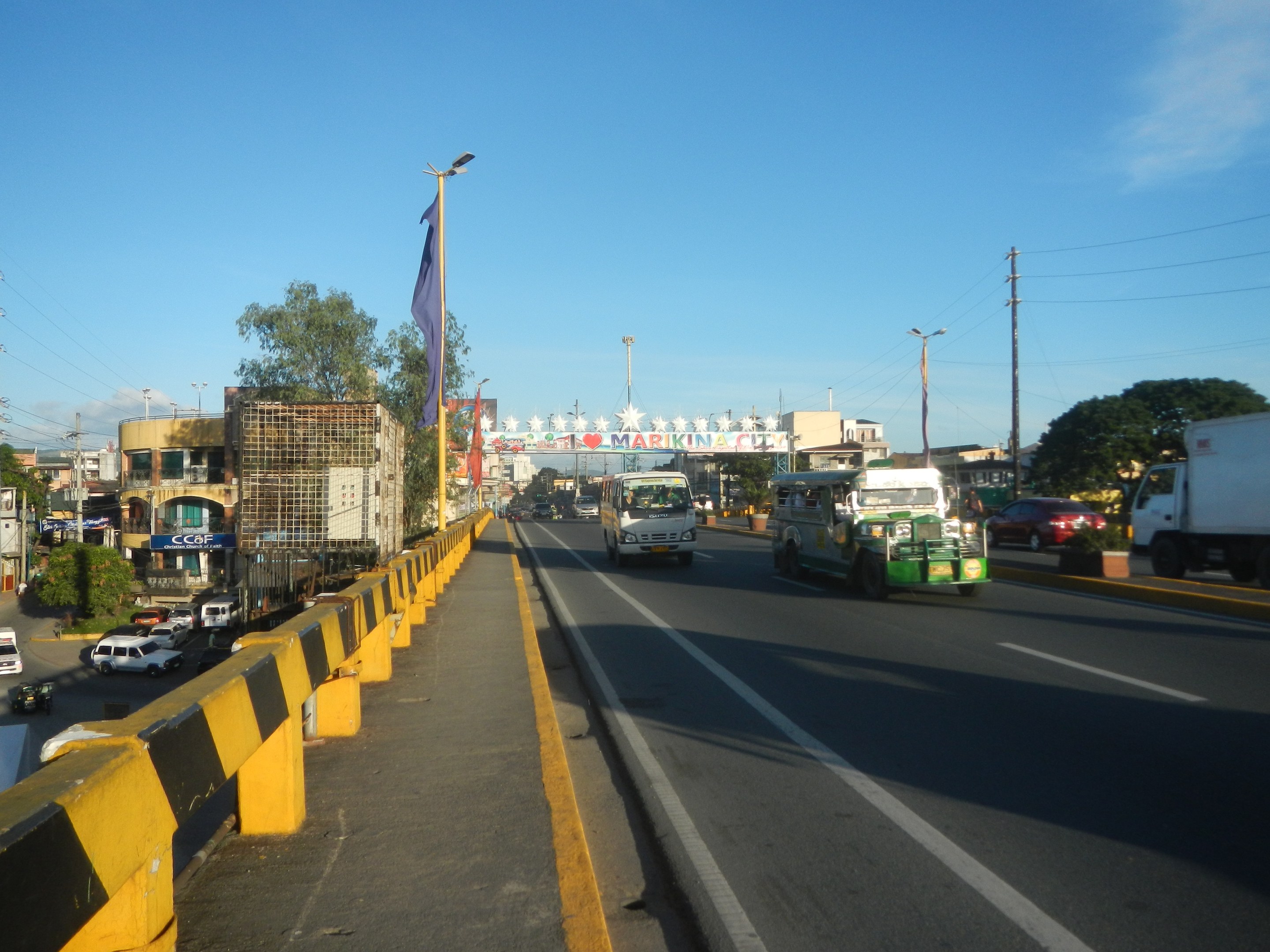 Eine stadtstraßen mit starkem verkehr, eine mittellinie, ein flaggenmast mit einer flagge, gebäude, bäume, elektrischen masten mit drähten und ein bewölkter himmel im hintergrund.