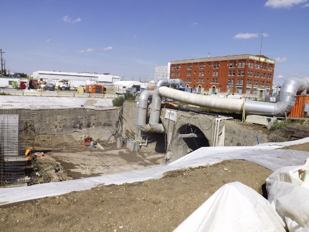 Eine Szene mit Geb├Ąuden, einem Zaun, Fahrzeugen, aktuellen Umfragen, einer Rohrleitung und dem Himmel ├╝ber ihnen.