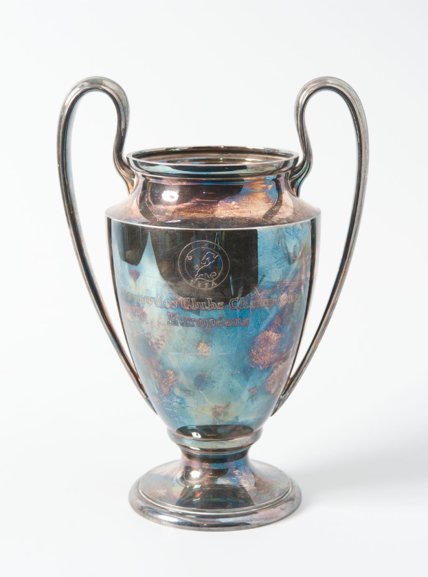 Der UEFA-Champions-League-Pokal, ein stählerner Becher mit zwei Griffen und einem blauen und silbernen Farbschema, der mit "UEFA Champions League" beschriftet ist, vor einem weißen Hintergrund dargestellt.