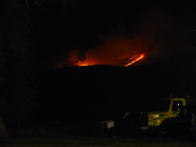 Ein Fahrzeug wird bei Nacht mit einem Feuer im Hintergrund gezeigt.