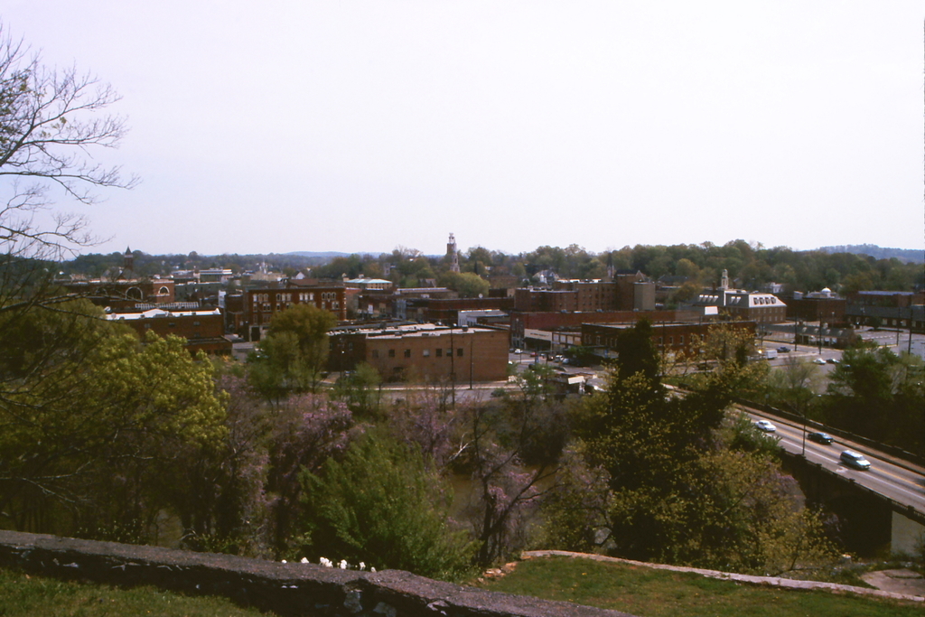 Eine Stadtansicht mit Gebäuden, Bäumen, Polen, Straßen, Fahrzeugen und Himmel.