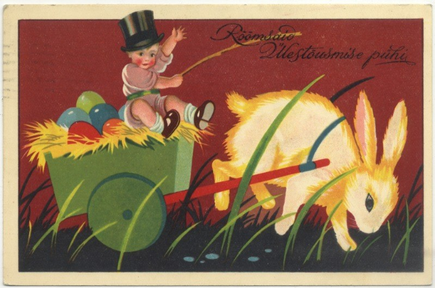 Alte Postkarte mit einem Baby in einem Zylinder, das einen Karren voller bunter Ostereier schiebt, begleitet von einem Kaninchen, mit handgeschriebenen Ostergrüßen.