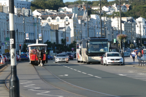 Eine belebte Stadtstraße mit hohen Gebäuden, Fahrzeugen, Fußgängern, Ampeln, Laternenmasten, Straßenschildern, Bäumen und einem klaren blauen Himmel.