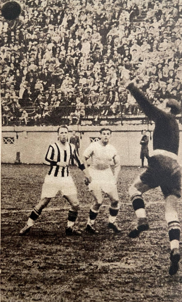 Ein Schwarz-Weiß-Foto von einer Gruppe von Männern, die auf einem Feld Fußball spielen, mit einer Zuschauermenge im Hintergrund und einer Wand dahinter. Unten auf dem Bild steht der Text "Newcastle United v West Bromwich Albion".