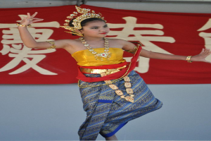 Ein Mädchen tanzt in traditioneller Kleidung und Schmuck, mit einem Banner im Hintergrund.