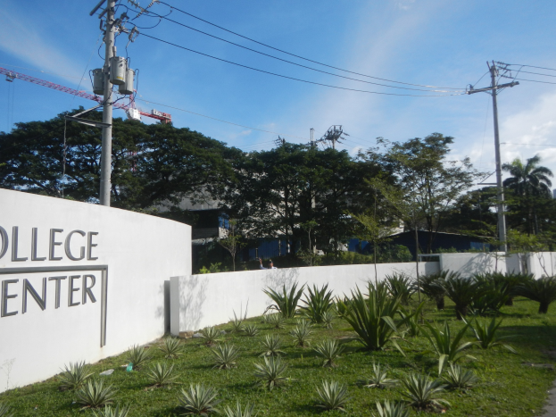 Eingang zu einem College-Center mit einem "College Center"-Schild an der Wand, umgeben von Grünfläche, einem Weg, Strommasten, Bäumen, Gebäuden und einem bewölkten Himmel.