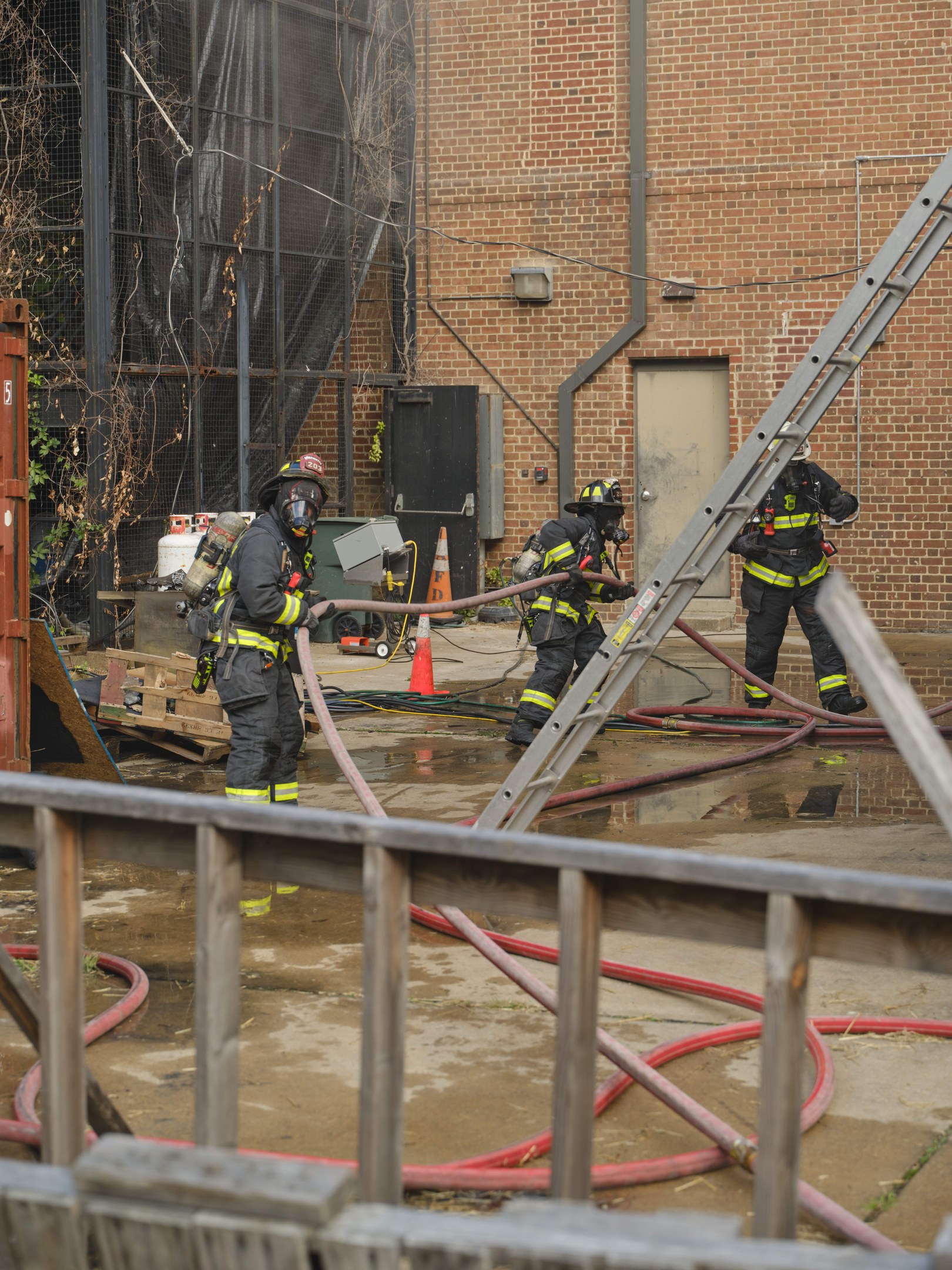 Feuerwehrleute in Helmen verwenden Schläuche, um ein Gebäude Feuer in der Nähe eines Metallzauns zu löschen.