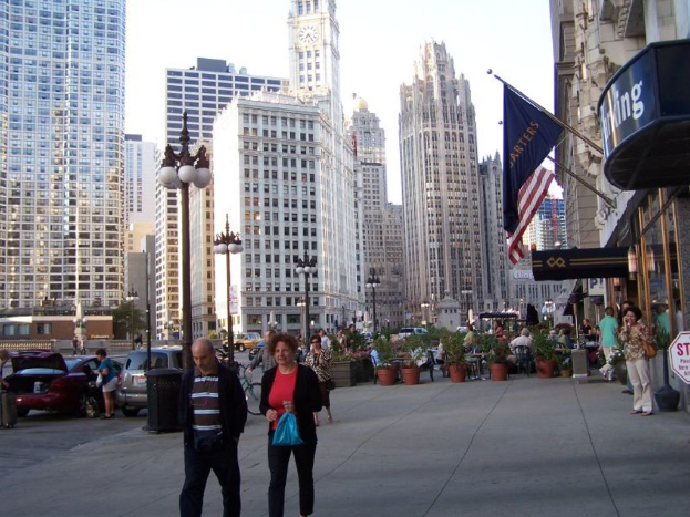 Eine belebte StraßenSzene mit Menschen, Blumenkisten, Autos, Straßenlaternen, Gebäuden, Geschäften und Fahnen im Hintergrund.