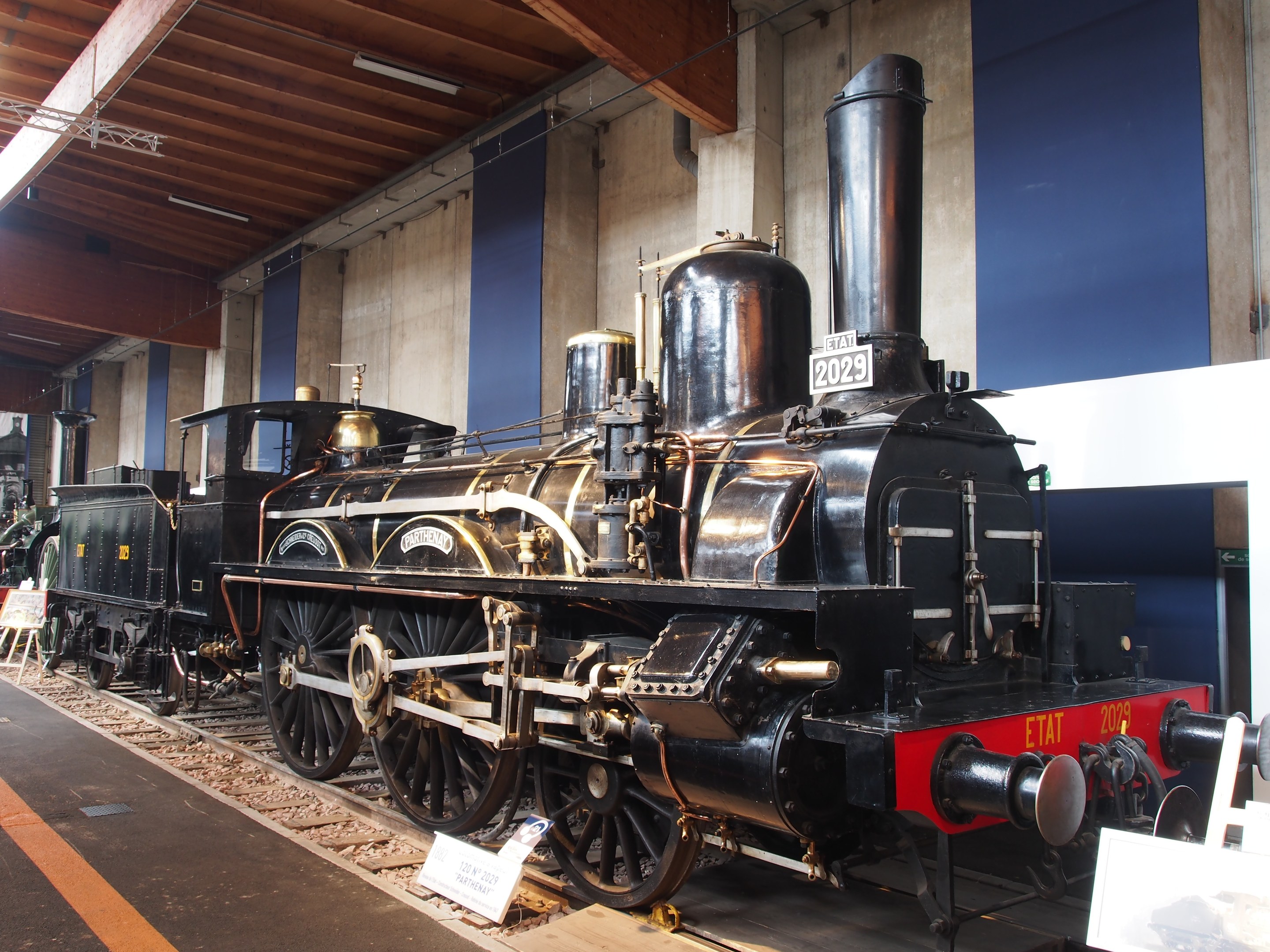 Alte Dampflokomotive in einem Museum ausgestellt, umgeben von Eisenbahnschienen und Informationsschildern.