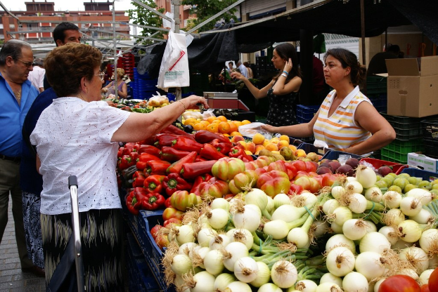 Kunststoffbehälter mit Gemüse gefüllt, eine Gruppe von Menschen in der Nähe von Gebäuden und Bäumen, eine Pappkiste und der Himmel.