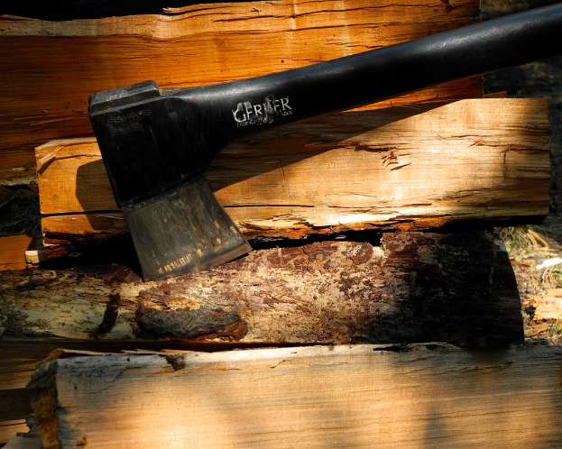 Eine schwarze Axt und mehrere Holzstücke liegen auf einer Oberfläche.