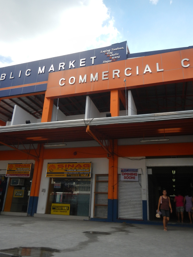 Öffentlicher Marktkomplex mit Menschen vor einem Gebäude mit Text, unter einem sichtbaren Himmel.