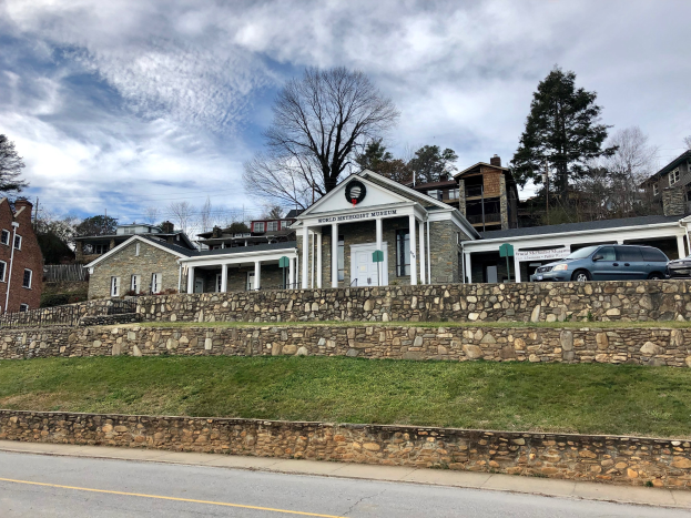 Steinwand mit parkenden Autos davor, flankiert von Gebäuden mit Fenstern und Türen, Bäumen und einem bewölkten Himmel, als das kürzlich wiedereröffnete Weltkulturerbe-Museum bezeichnet.