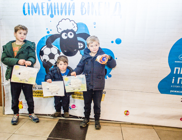 Drei Kinder halten Papiere vor einem Banner in den Händen