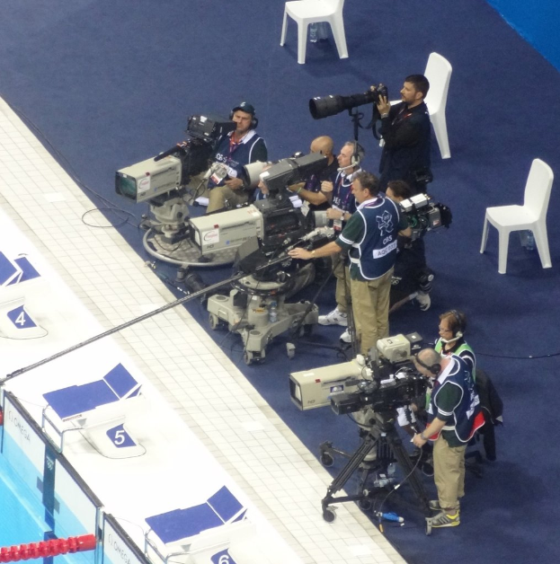 Eine Gruppe von Menschen mit Kameras, wobei im Hintergrund mehrere Stühle sichtbar sind.