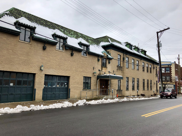 Ein groes Ziegelsteingebäude mit einem grünen Dach an einer Straßenecke, umgeben von Fahrzeugen, Schnee, Strommasten, Bäumen und einem bewölkten Himmel, identifiziert als das ehemalige St. Louis Fire Station.