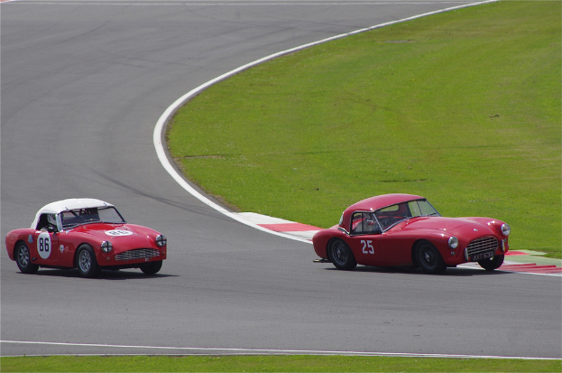 Zwei rote Autos auf einer Rennbahn mit einer Grasfläche auf der rechten Seite.
