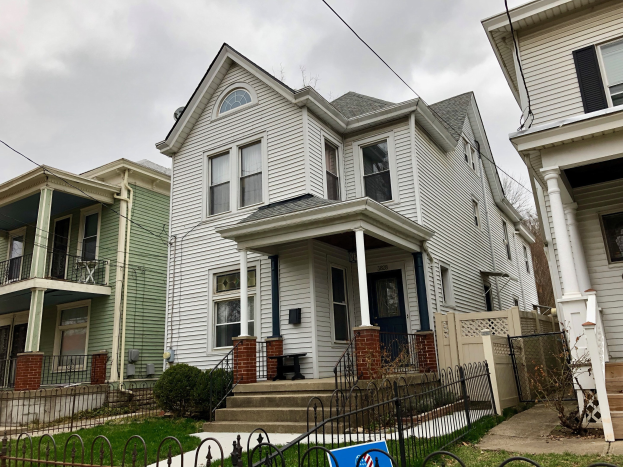 Reihe von Mietshäusern mit Fenstern, Türen, Säulen, Geländern, Stufen und Dächern, umgeben von einem Metallzaun, Gras, Pflanzen, Bäumen und einem bewölkten Himmel, mit einem Mietschild, das die Adresse 5901 S Elmwood Ave, Chicago 60618 anzeigt.