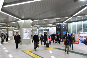 Menschen mit Gepäck durch einen Bahnhof gehen, überirdische Schilder und Deckenleuchten.