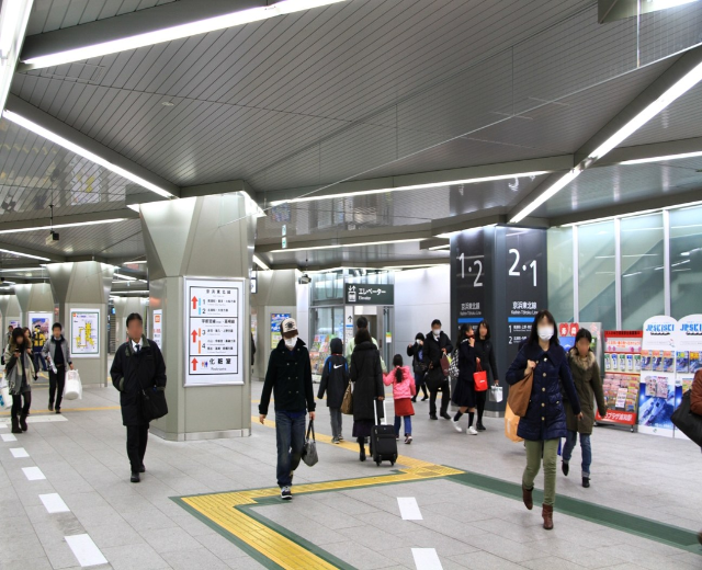 Menschen mit Gepäck durch einen Bahnhof gehen, überirdische Schilder und Deckenleuchten.