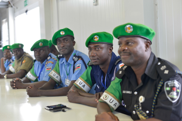 Polizeibeamte sitzen an einem Tisch während einer Schulung, mit Mobiltelefonen und anderen Gegenständen auf dem Tisch, in einem Raum mit Fenstern und Deckenbeleuchtung.