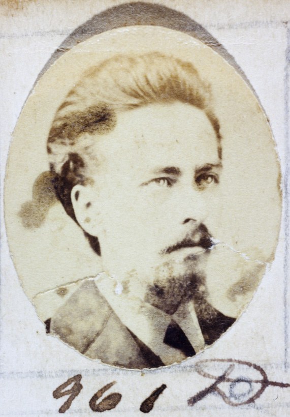 Ein Schwarz-Weiß-Porträt eines älteren Mannes mit Schnurrbart und Vollbart, der einen Anzug und eine Krawatte trägt und direkt in die Kamera schaut.