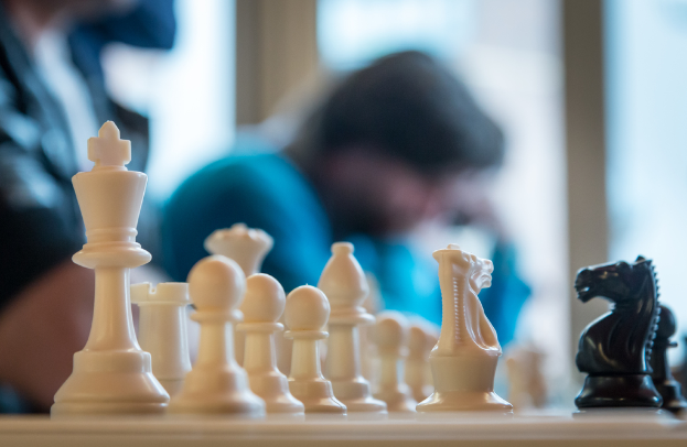 Mehrere Schachfiguren und einige Personen im Hintergrund.