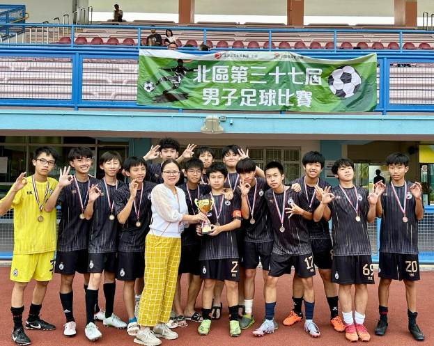 Gruppe junger Männer in Fußballtrikots auf einem Feld mit einem Pokal und Medaillen, im Hintergrund ein Banner mit der Aufschrift "Yokohama U-16 Jungenfußballmannschaft"