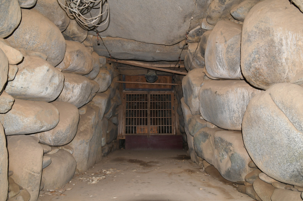 Ein tunnel voller Steine und ein Metalltor in der Mitte, mit Drähten, die an der Decke entlanglaufen, ähnlich wie ein Stolleneingang.