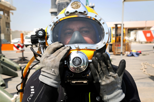 Eine Person in Handschuhen und einem Feuerwehrhelm steht vor einer Szene mit Fahrzeugen, Gebäuden, Häusern, Pfählen und verschiedenen Gegenständen unter einem Himmel.