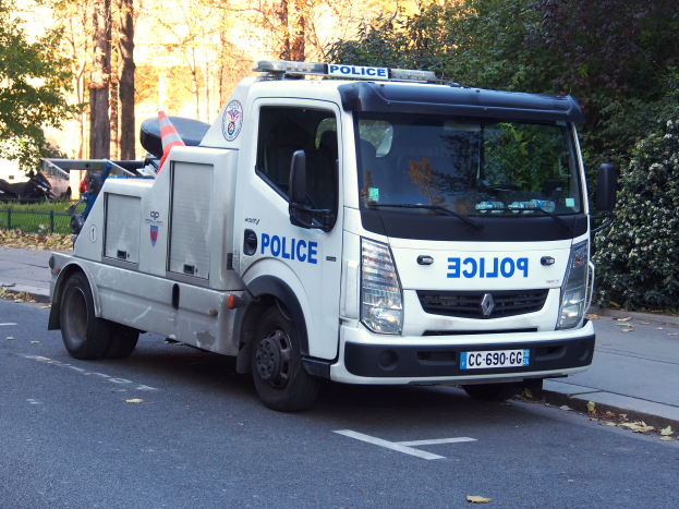Polizeilaster am Straßenrand mit Bäumen, Pflanzen, Gras, einem Zaun und einem Gebäude im Hintergrund geparkt.