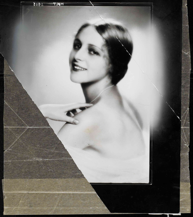 Schwarzes und weißes Porträt einer Frau in einem Kleid im Stil der 1920er Jahre mit ihrem Haar zu einem ordentlichen Knoten gebunden, die warm in die Kamera lächelt.