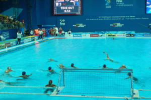 Gruppe von Menschen, die Wasserball in einem Pool während der 2015 FINA World Championships in Kazan spielen, mit Zuschauern und Eventwerbung im Hintergrund.
