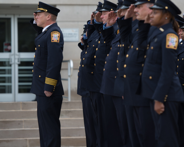 Gruppe von Polizisten in Uniform, die in Formation salutieren, vor einem Gebäude mit Glastüren und Treppe.