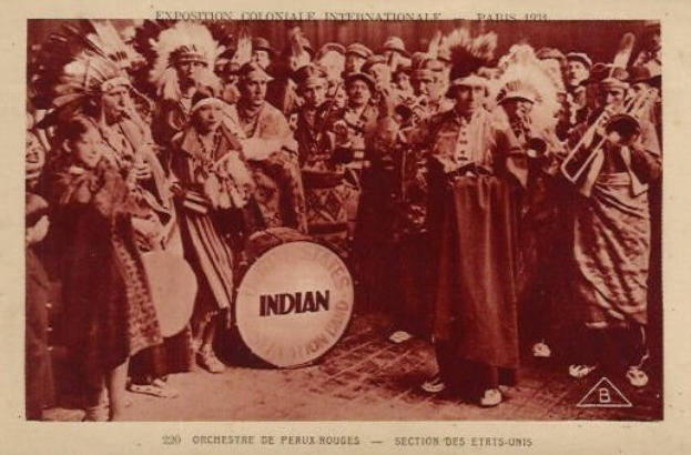 Gruppe von Menschen in Kostuemen mit Musikinstrumenten und einer Trommel in der Mitte, altes Foto-Stil, mit Text und Logo unten.