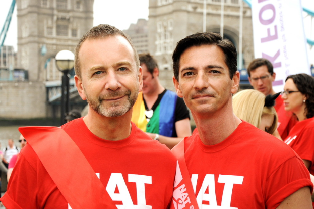 Zwei Personen in orangen T-Shirts stehen vor Geb√§uden.