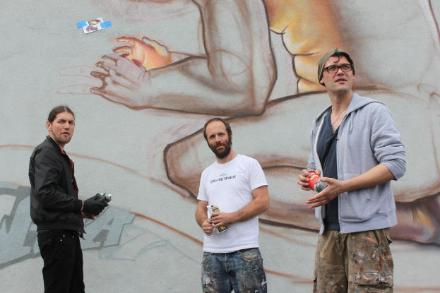 Menschen mit Farbsprühflaschen in der Hand vor einer Graffiti-Wand