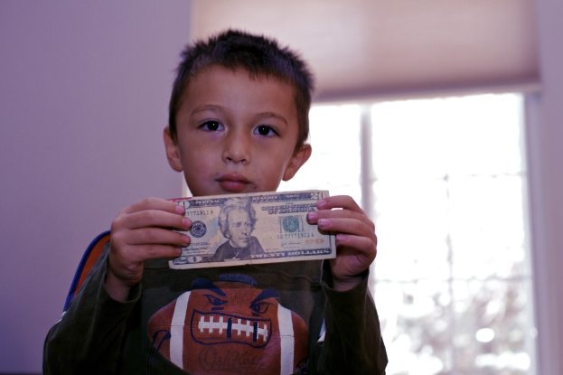 Ein Junge hält Geld in den Händen, im Hintergrund ein Fenster und eine Wand.