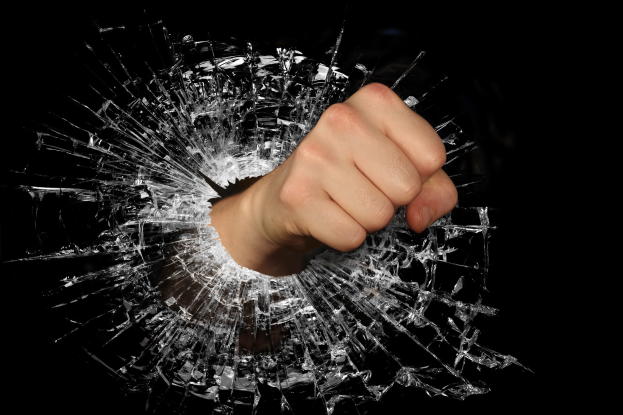 Eine Hand, die durch zerbrochenes Glas auf einem schwarzen Hintergrund bricht.