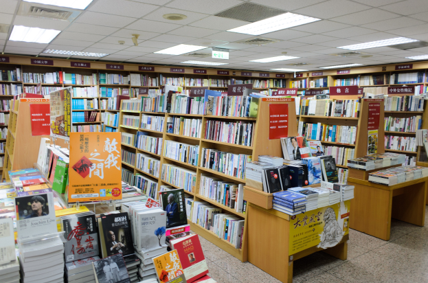 Ein gut organisierter Buchladen mit ordentlich aufgestellten Bücher auf Regalen und Tischen, mit informativen Schildern auf dem Boden und Deckenlampen.