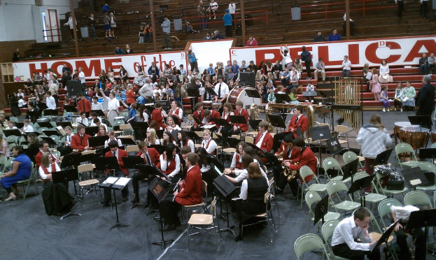 Eine Gruppe von Kindern, die auf Stühlen in einem Stadion für einen Musikunterricht sitzen, mit sichtbaren Stadionplätzen im Hintergrund.