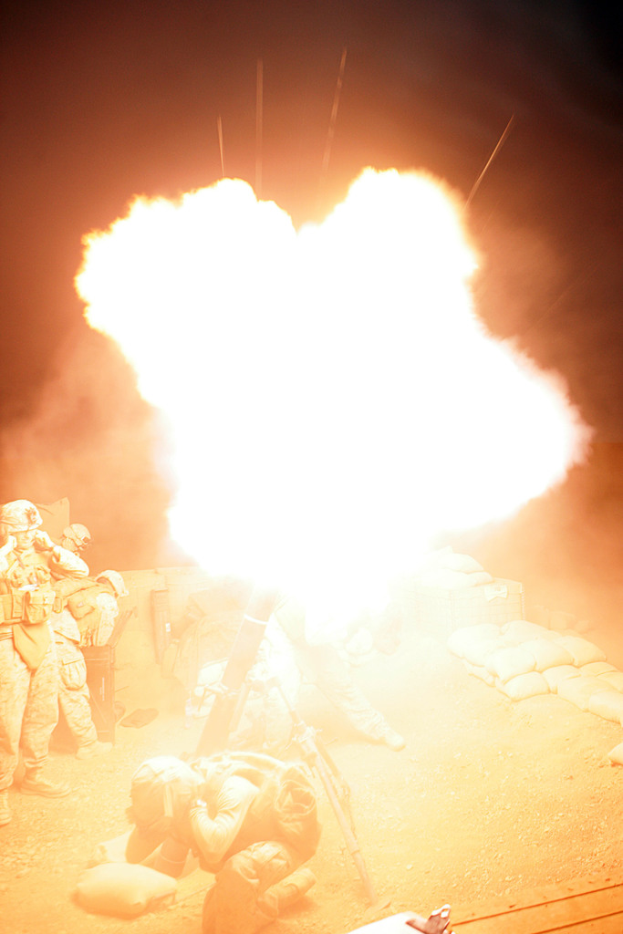 Mehrere Personen in Uniformen und Helmen auf einem Gelände mit einigen Taschen, mit einem Feuer in der Mitte der Szene.