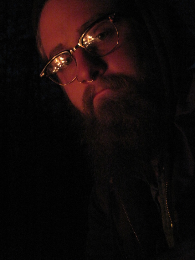 Ein Mann mit einem großen Bart und Brille posiert für die Kamera in einer Nahaufnahme.