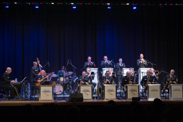 Eine Gruppe von Musikern performs auf einer hell erleuchteten Bühne mit der Aufschrift "The New Orleans Jazz Band", während das Publikum darunter zusieht.