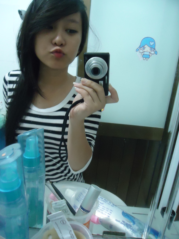 Eine Frau steht vor einem Schminktisch mit Kosmetika und macht ein Foto mit einer Kamera, im Hintergrund ist eine Tür zu sehen.