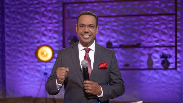 Stephen Colbert, Moderator von 'The Daily Show with Trevor Noah', steht auf einer Bühne und hält ein Mikrofon, trägt einen Anzug, Krawatte und eine Brille, mit einem Scheinwerfer und Ständer hinter ihm.